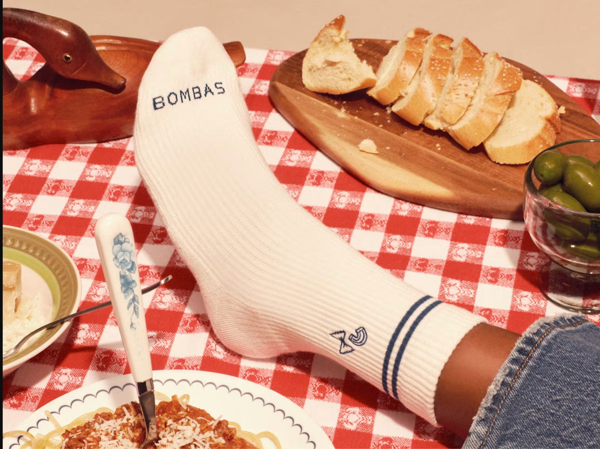 A white ribbed sock on a red checked tablecloth, beside sliced bread and olives
