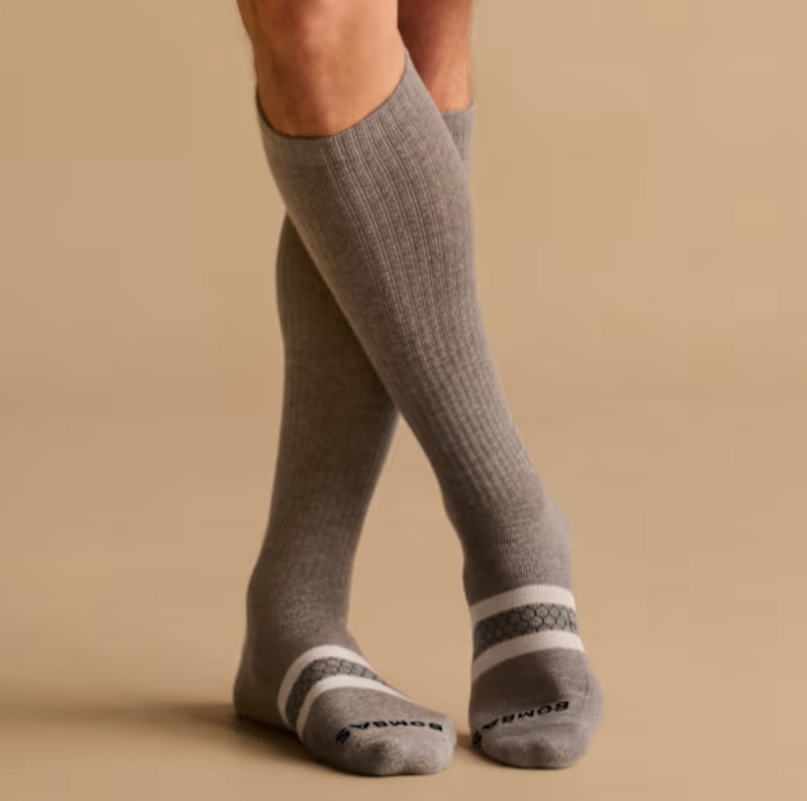 Legs in grey knee-high compression socks, seen against a plain backdrop