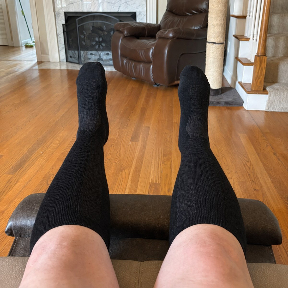 Customer photo from Nathalia D. — black knee high compression socks, feet up on a footrest at home